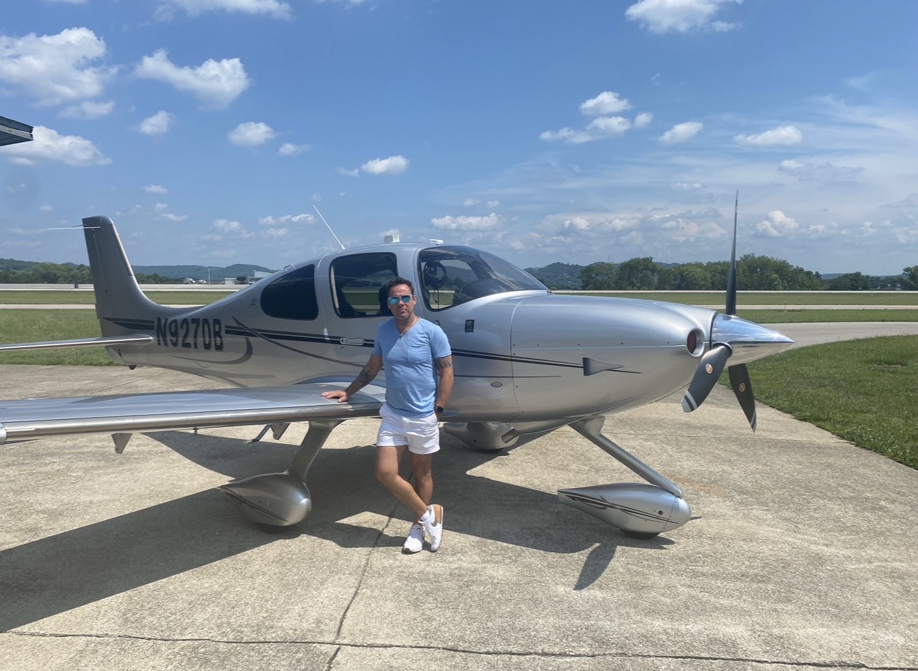 Black and white photograph of Anton Payne standing beside a Cirrus aircraft on the tarmac